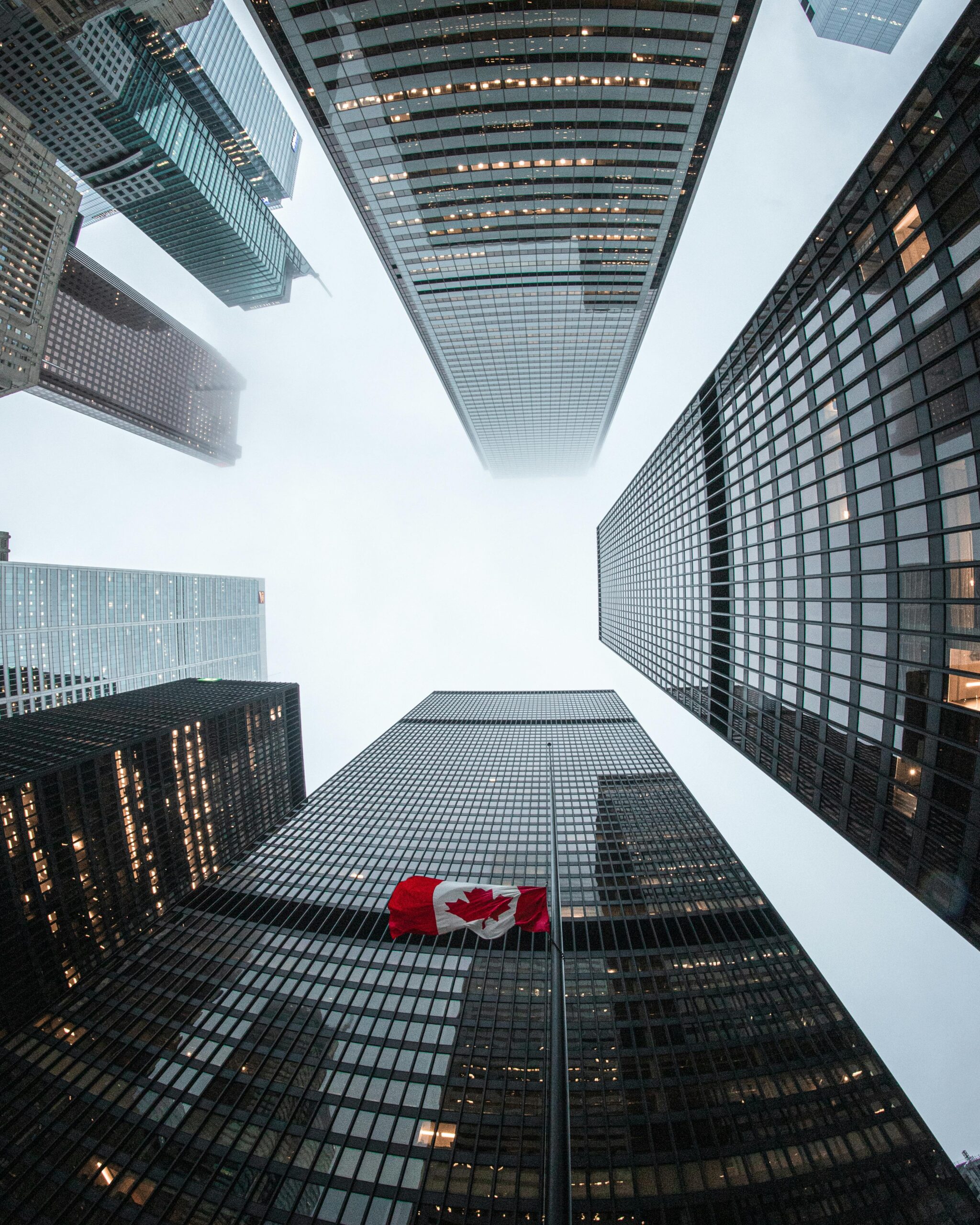 Looking up at Toronto skyscrapers with a Canadian flag on a cloudy day.