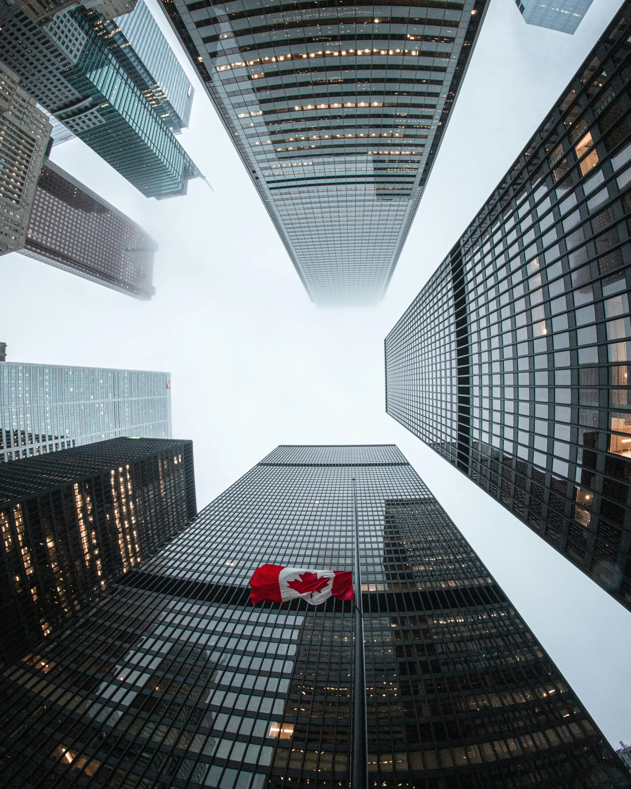 Looking up at Toronto skyscrapers with a Canadian flag on a cloudy day.