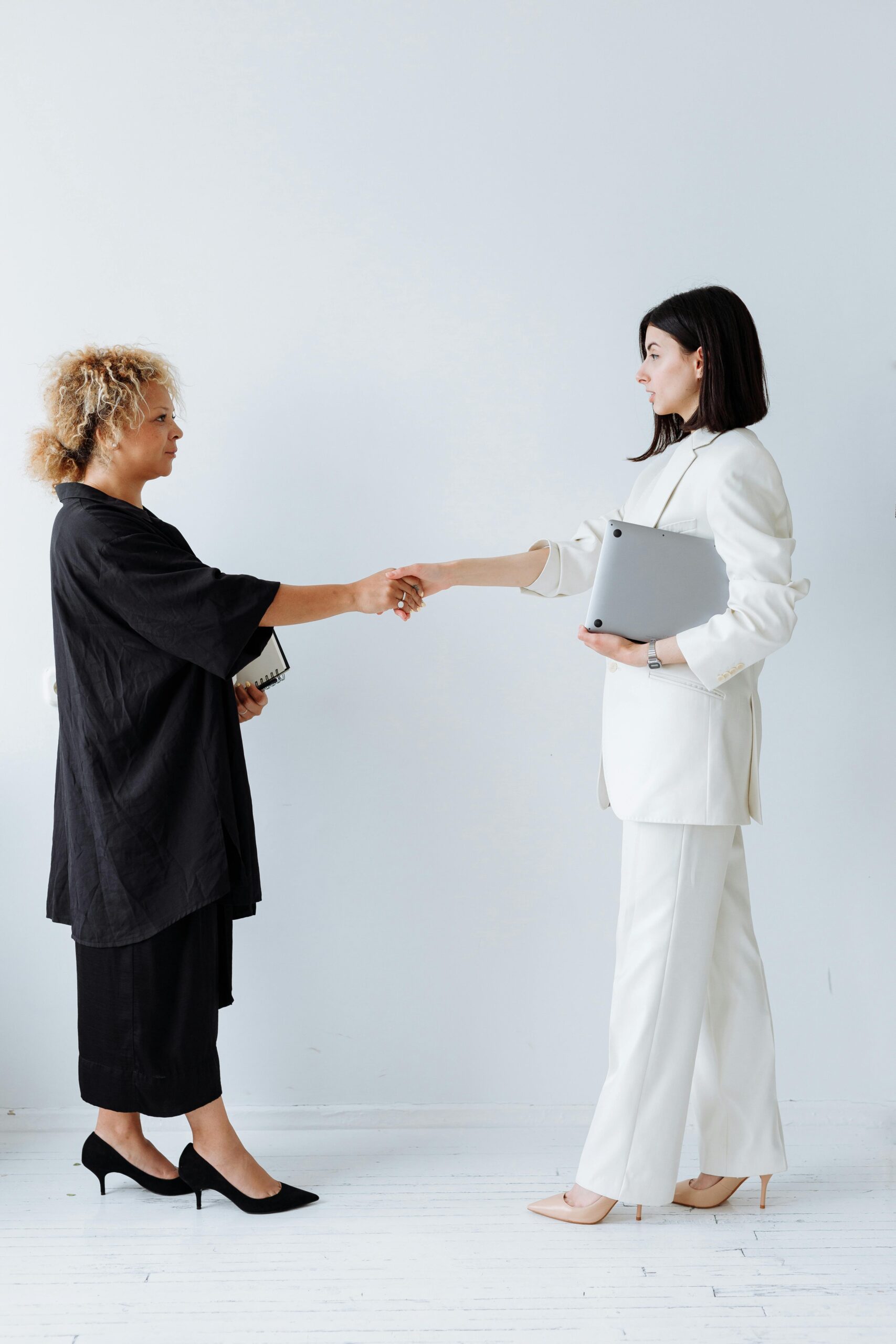 Two businesswomen shaking hands in an office setting, symbolizing partnership and teamwork.