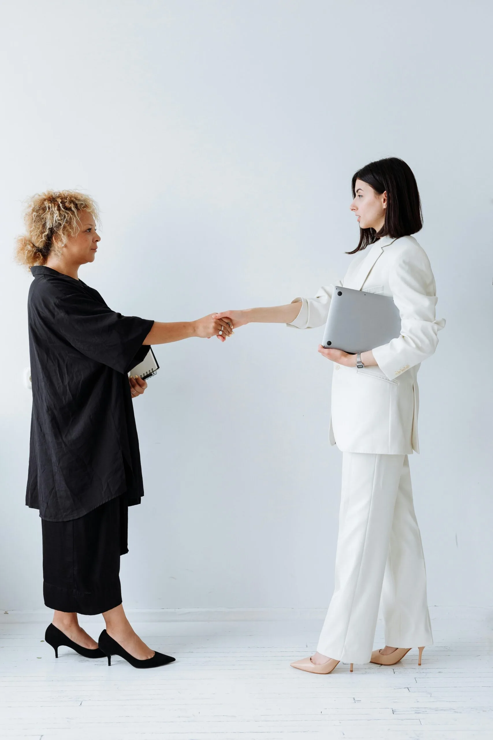 Two businesswomen shaking hands in an office setting, symbolizing partnership and teamwork.